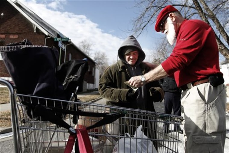 Secret Santa II hands a $100 bill to Robert Wright as he pushed a shopping cart down a street Tuesday in Kansas City.